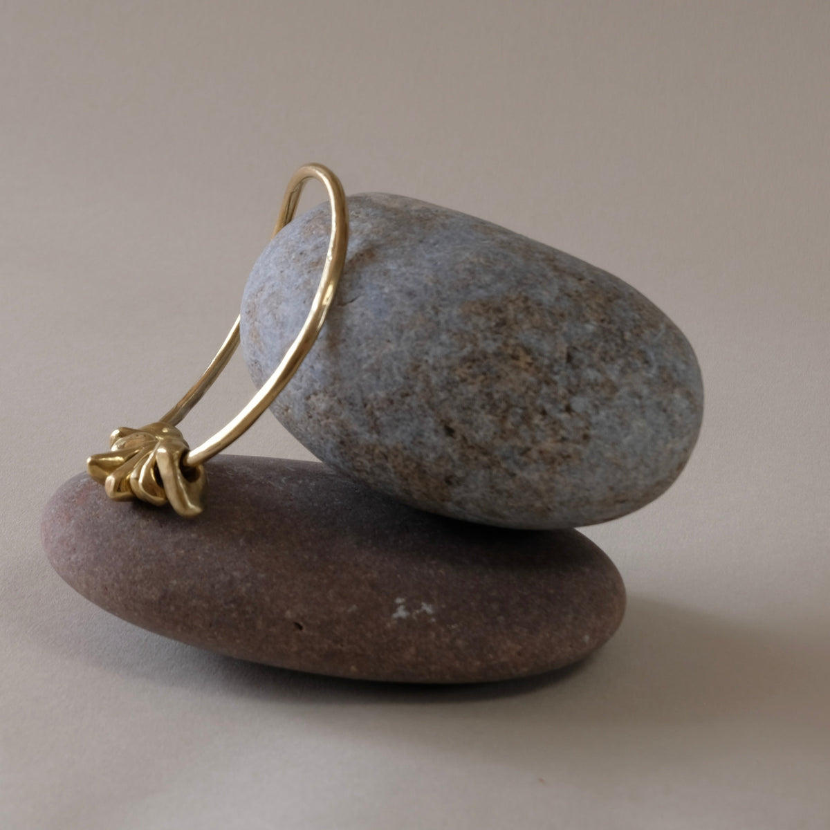 A gold hoop bangle with a textured, organic loop and pebbel charms,