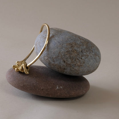 A gold hoop bangle with a textured, organic loop and pebbel charms,